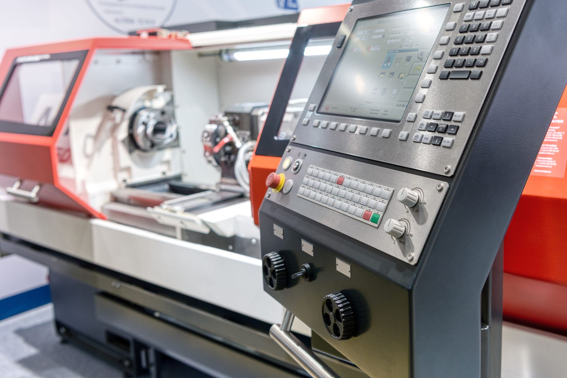 A red and white CNC lathe machine with a foreground control panel featuring a digital display and physical keypad.
