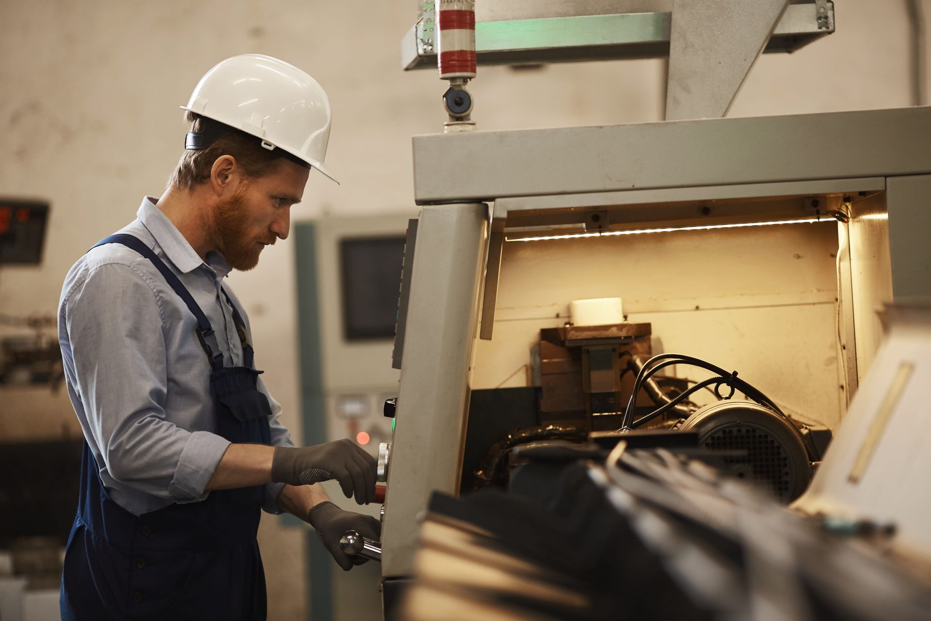 A person wearing a white hard hat and work uniform operates machinery in a factory setting.