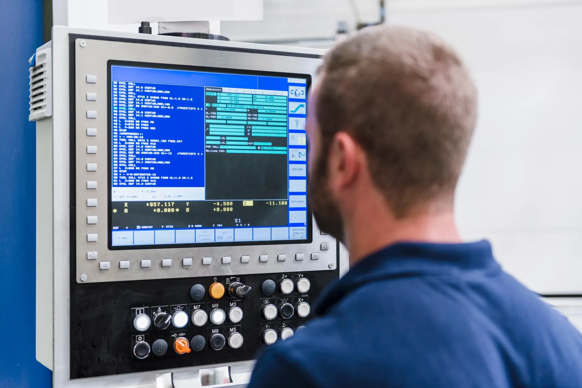 A person in a blue shirt operating a CNC machine control panel with a digital display and various buttons.