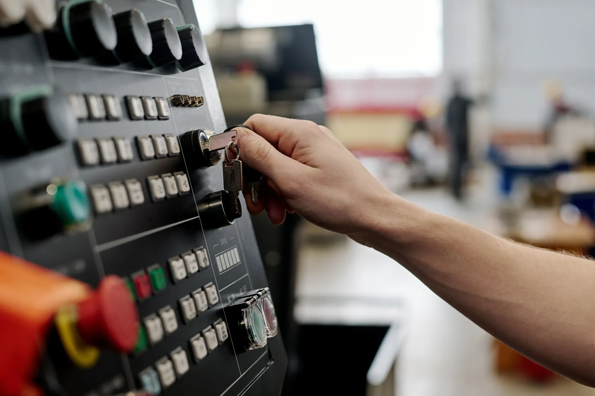 A hand turns a key in the control panel of an industrial machine within a workshop setting.