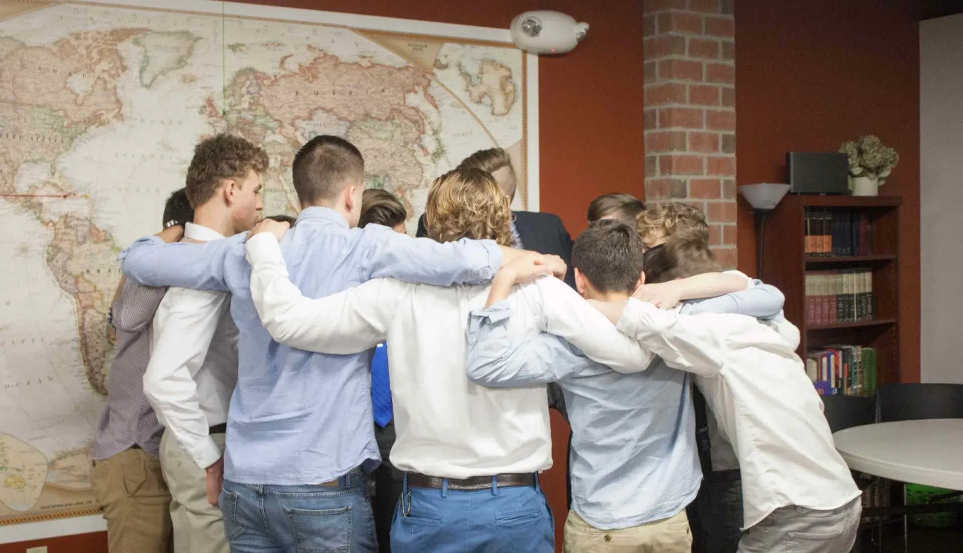 Group of people with arms around each other, standing in front of a world map in a room.