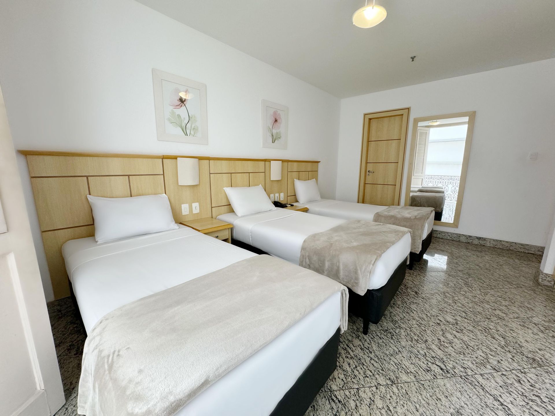 Um quarto de hotel com três camas e um espelho.