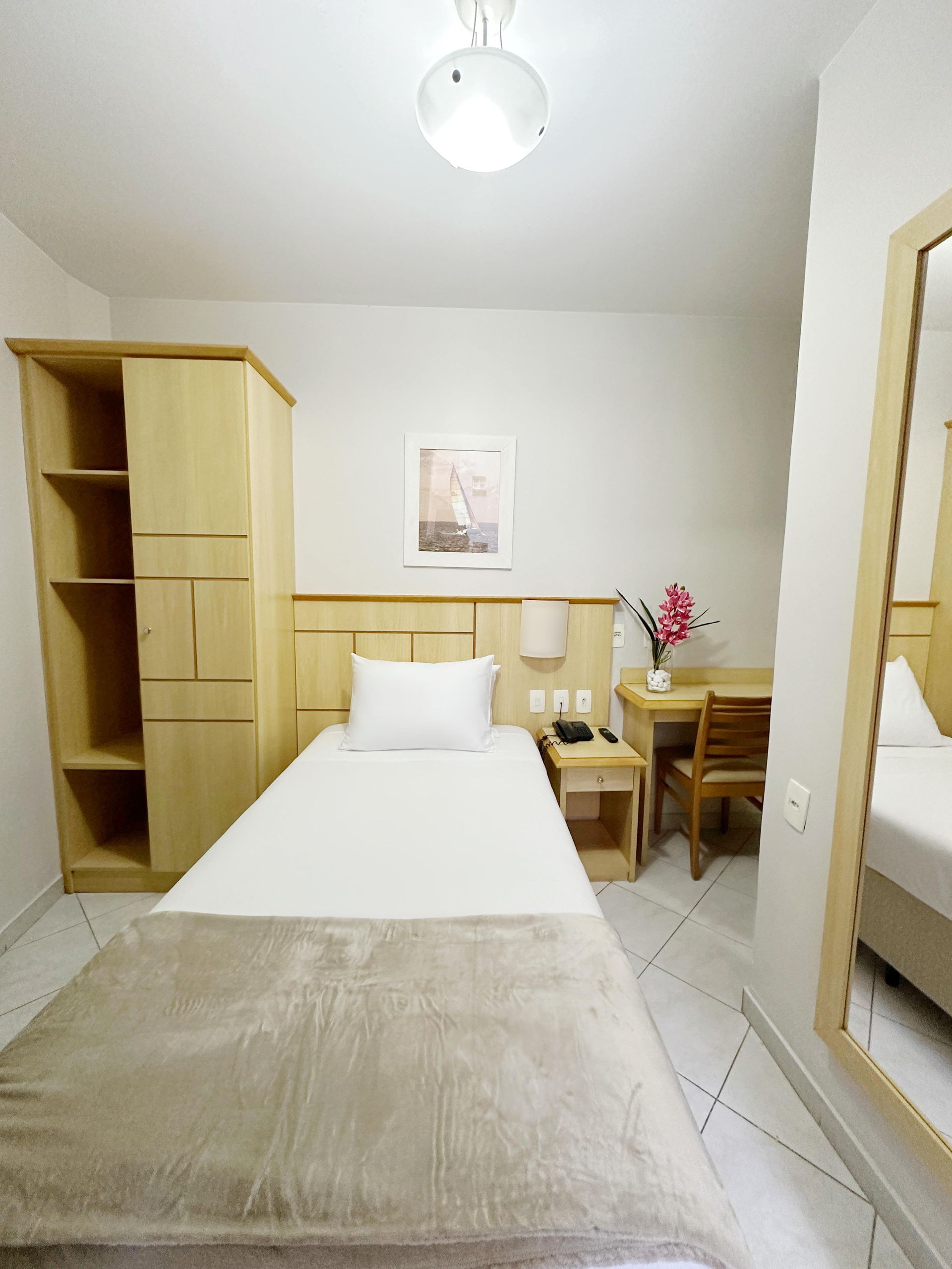 Um quarto de hotel com uma cama de solteiro e um espelho