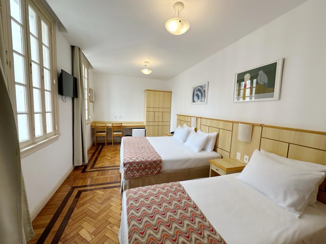 Um quarto de hotel com duas camas, uma escrivaninha e uma televisão.