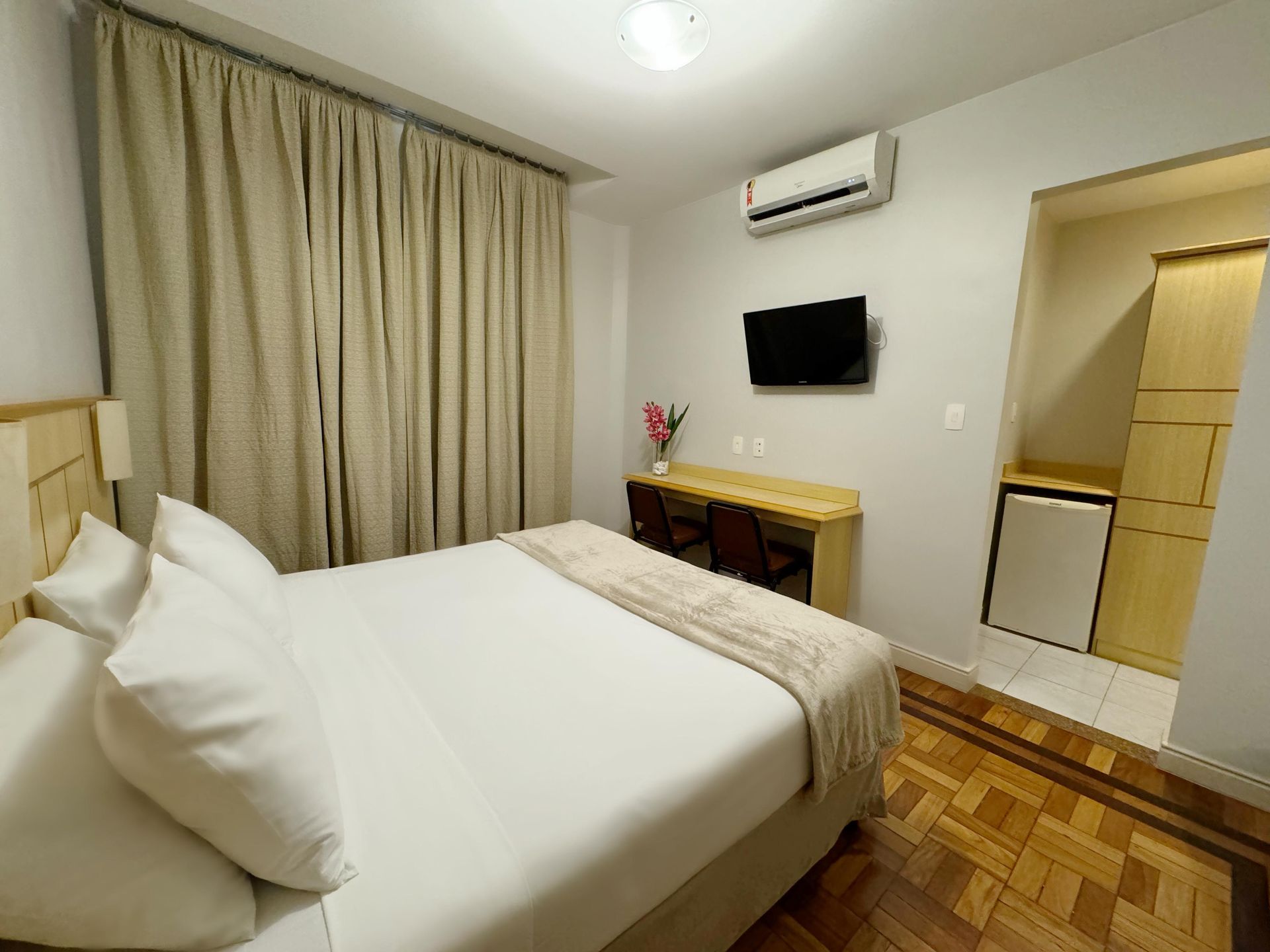 Um quarto de hotel com uma cama, escrivaninha e televisão.