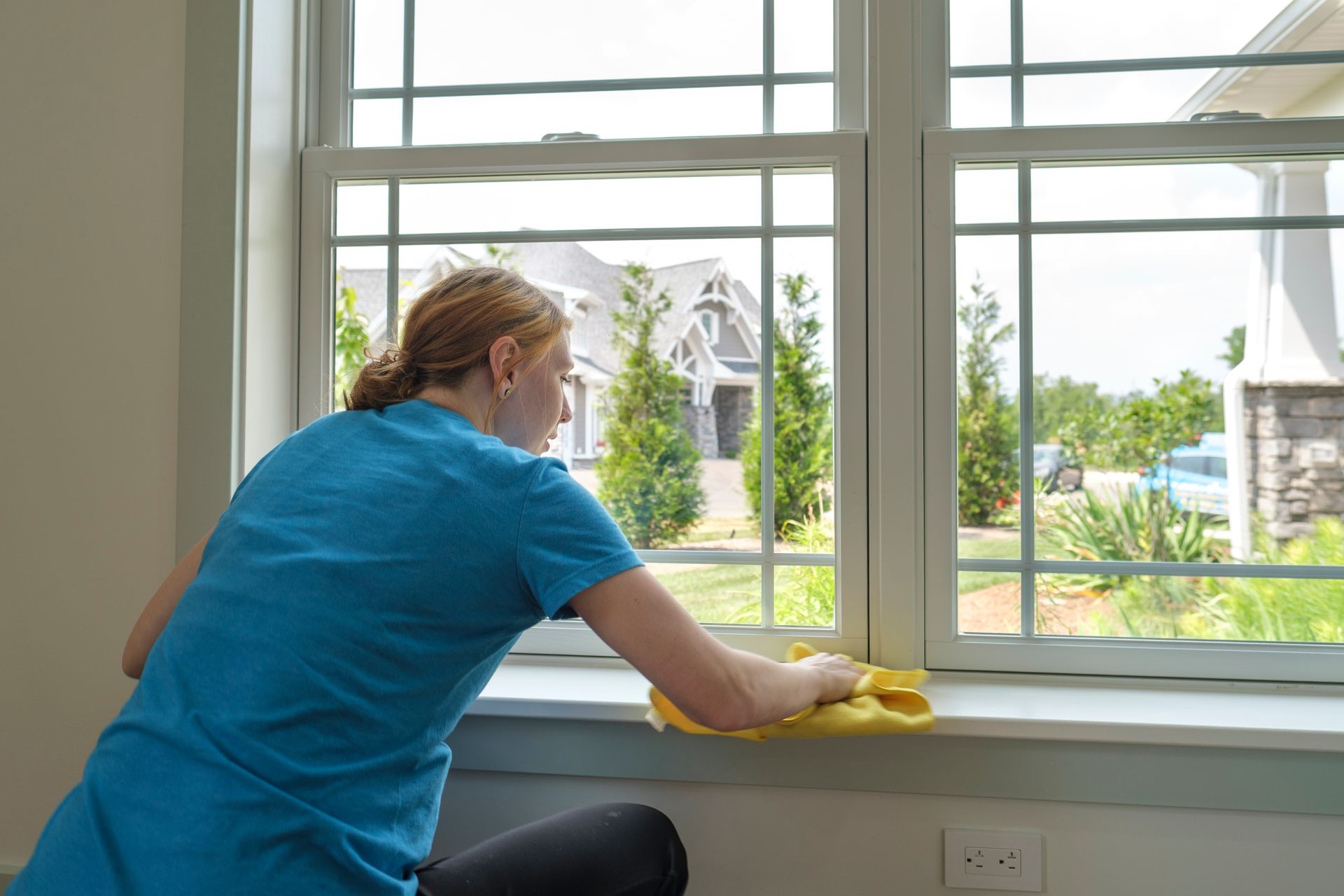 Woman cleaning window sill with yellow cloth.
