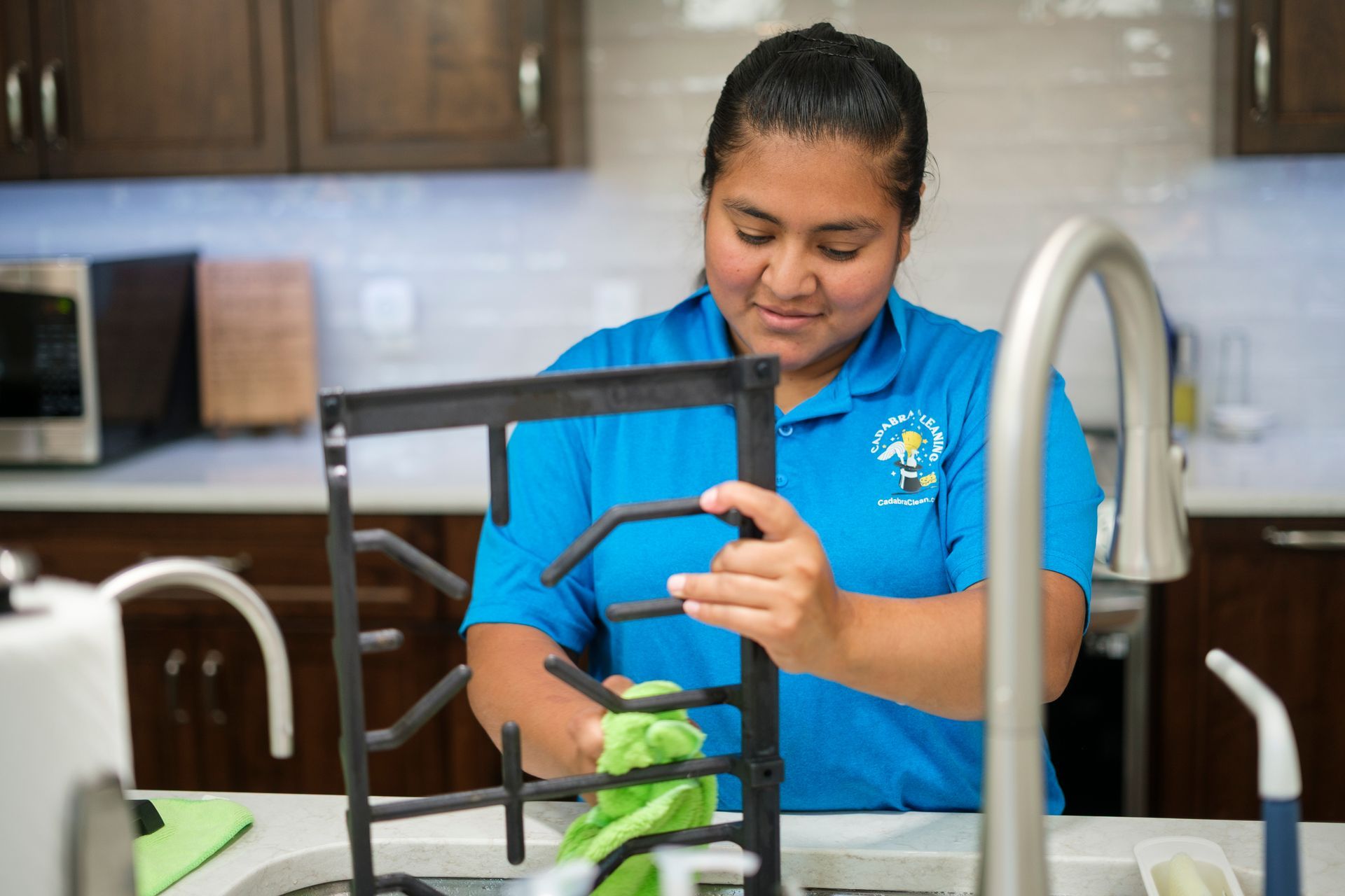 Woman in blue shirt cleaning a black rack in a kitchen sink.