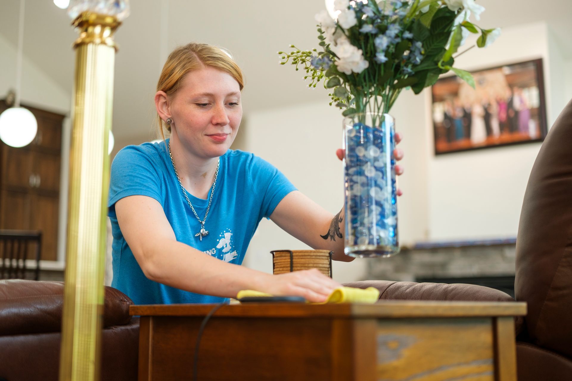 Woman dusting a table, vase of flowers, indoors.