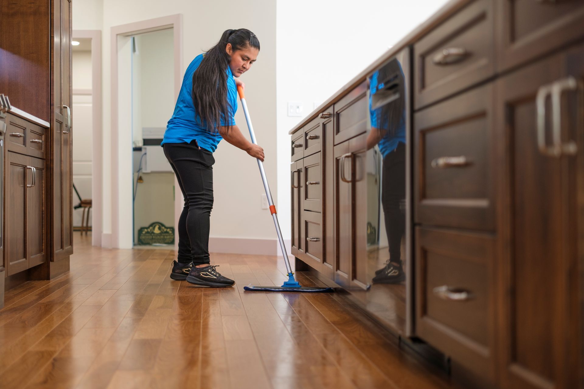 Person mopping a hardwood floor in a kitchen with dark cabinets.