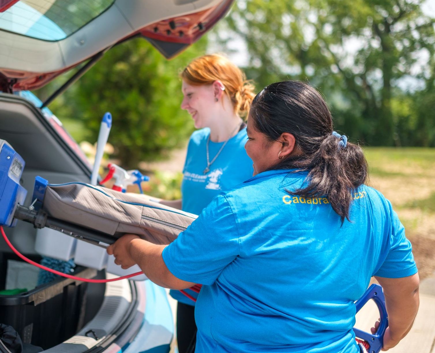Two people are unloading cleaning tools from a car.