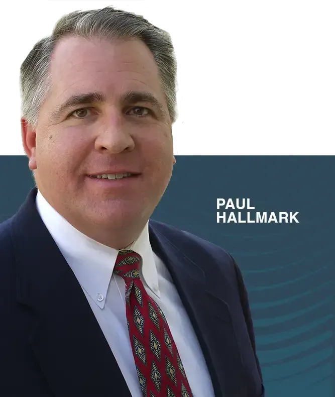 Professional headshot of Paul Hallmark in a suit and tie, set against a dark blue background with abstract wave patterns.