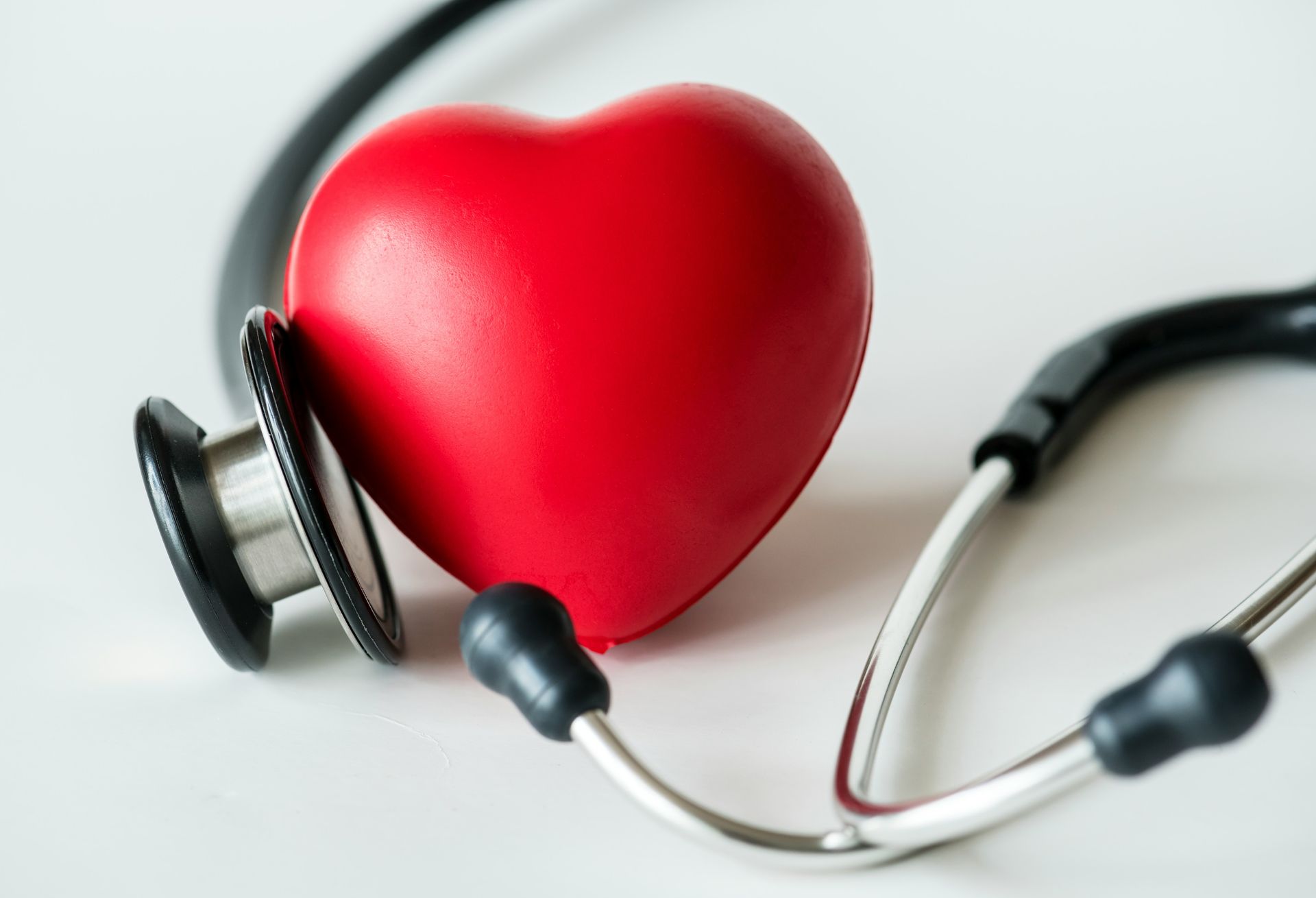 A bright red heart-shaped object resting next to a medical stethoscope on a white surface.