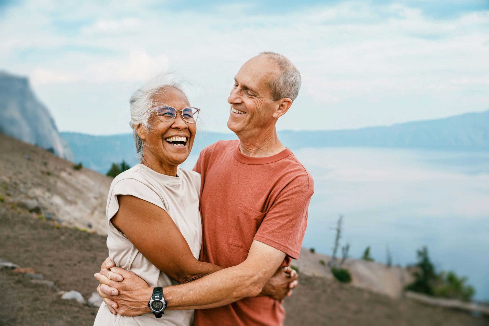 Two people embracing and smiling while overlooking a large lake and mountain landscape.