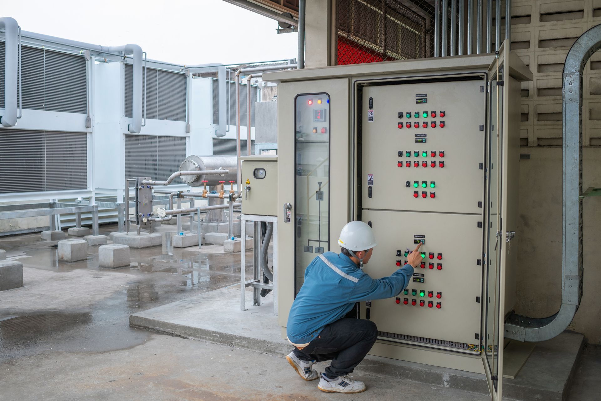 Worker crouching beside an industrial control panel in a factory setting, adjusting switches. Worker crouching beside an industrial control panel in a factory setting, adjusting switches.