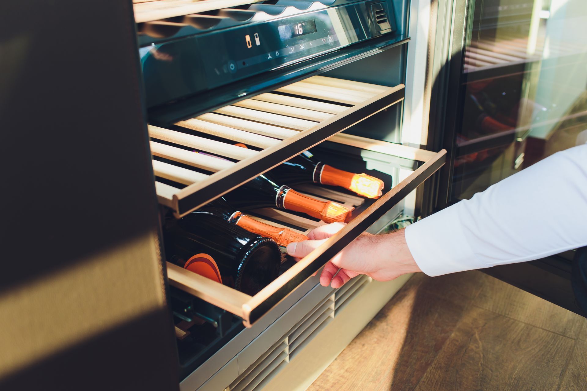 Hand reaching into an open wine cooler, selecting a bottle from a chilled rack Hand reaching into an open wine cooler, selecting a bottle from a chilled rack