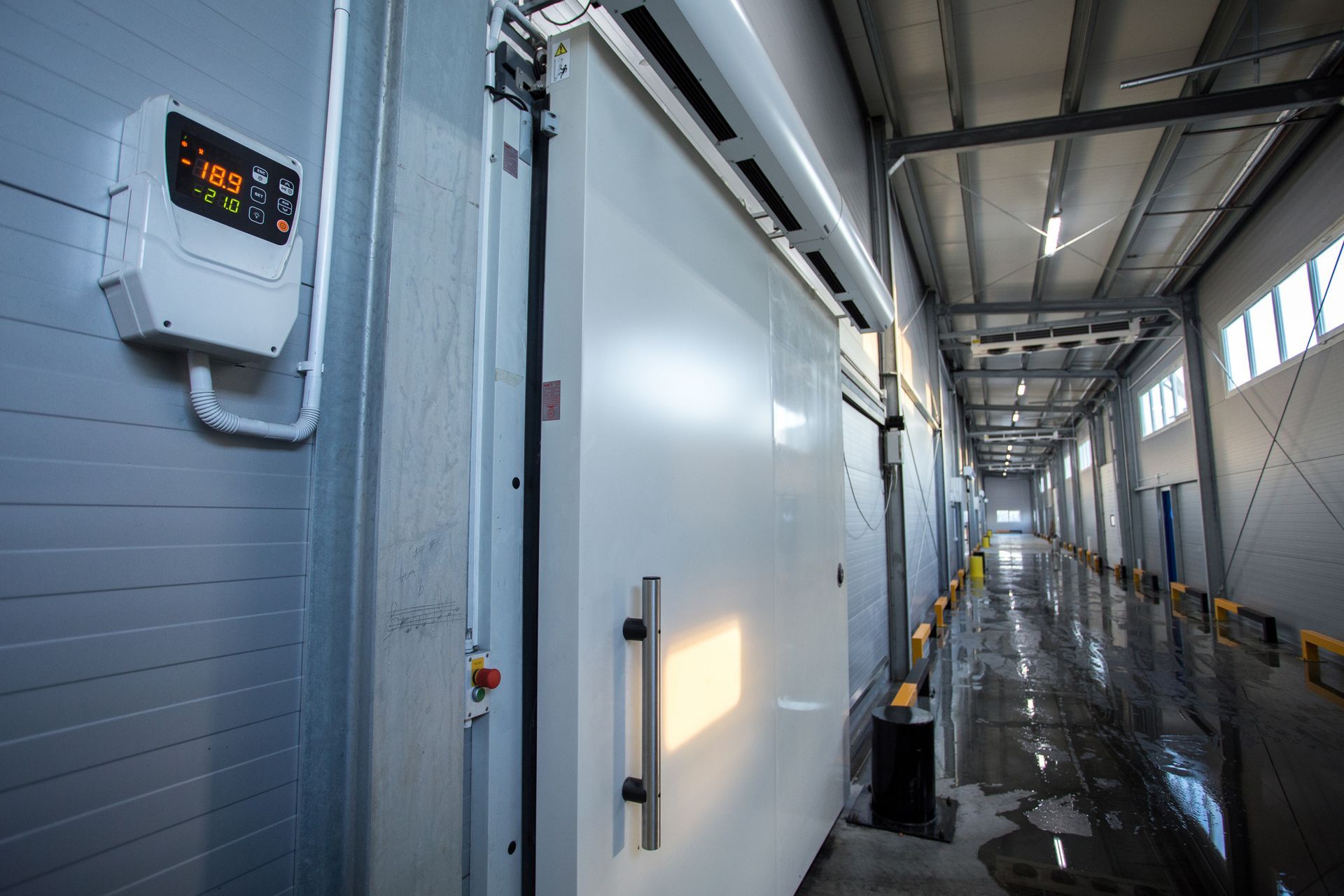 Industrial hallway with large white doors, overhead lights, and wet reflective floor inside a facility Industrial hallway with large white doors, overhead lights, and wet reflective floor inside a facility