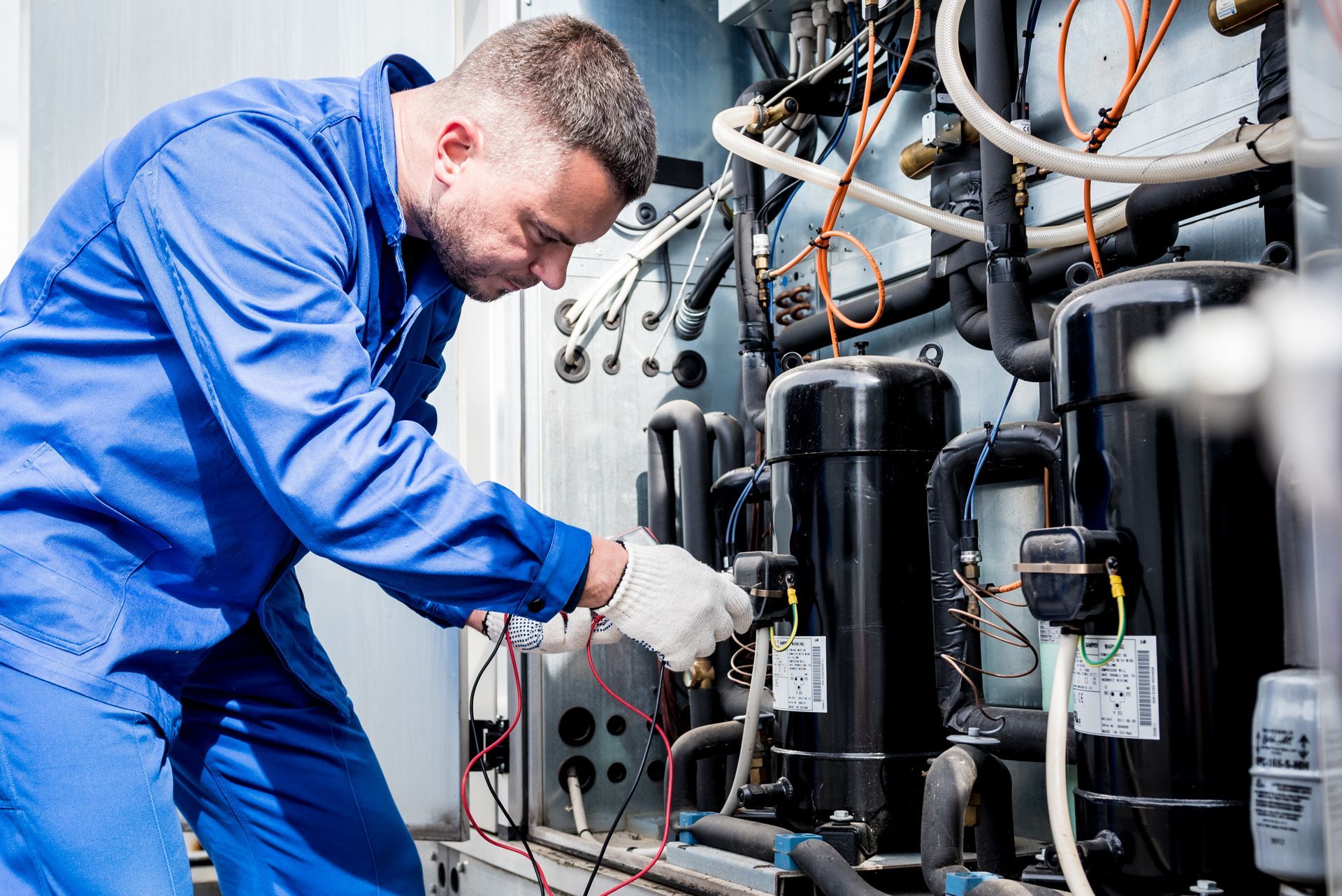 Technician in blue coveralls inspecting industrial HVAC equipment with gauges and pipes Technician in blue coveralls inspecting industrial HVAC equipment with gauges and pipes