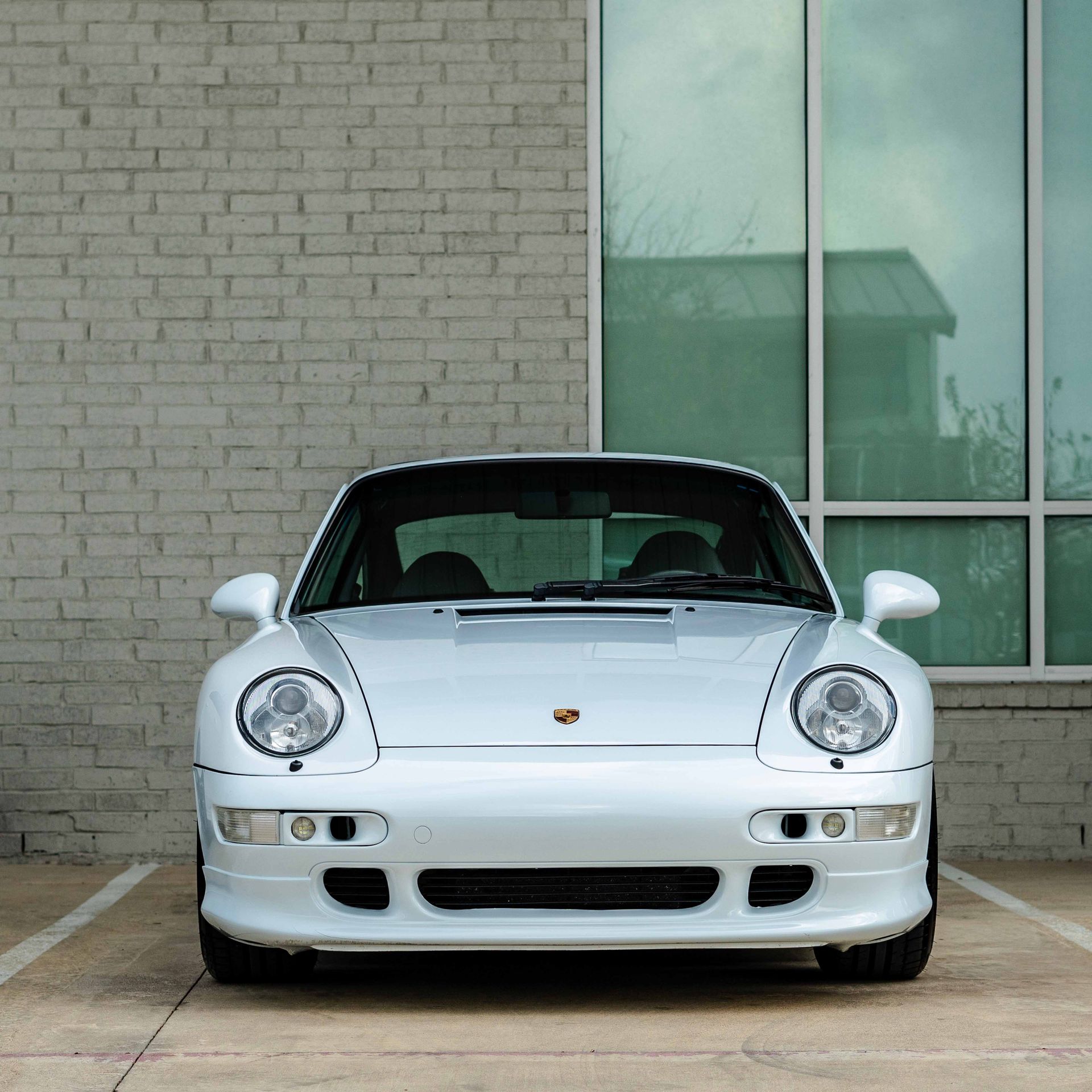 A white sports car is parked in front of a brick building