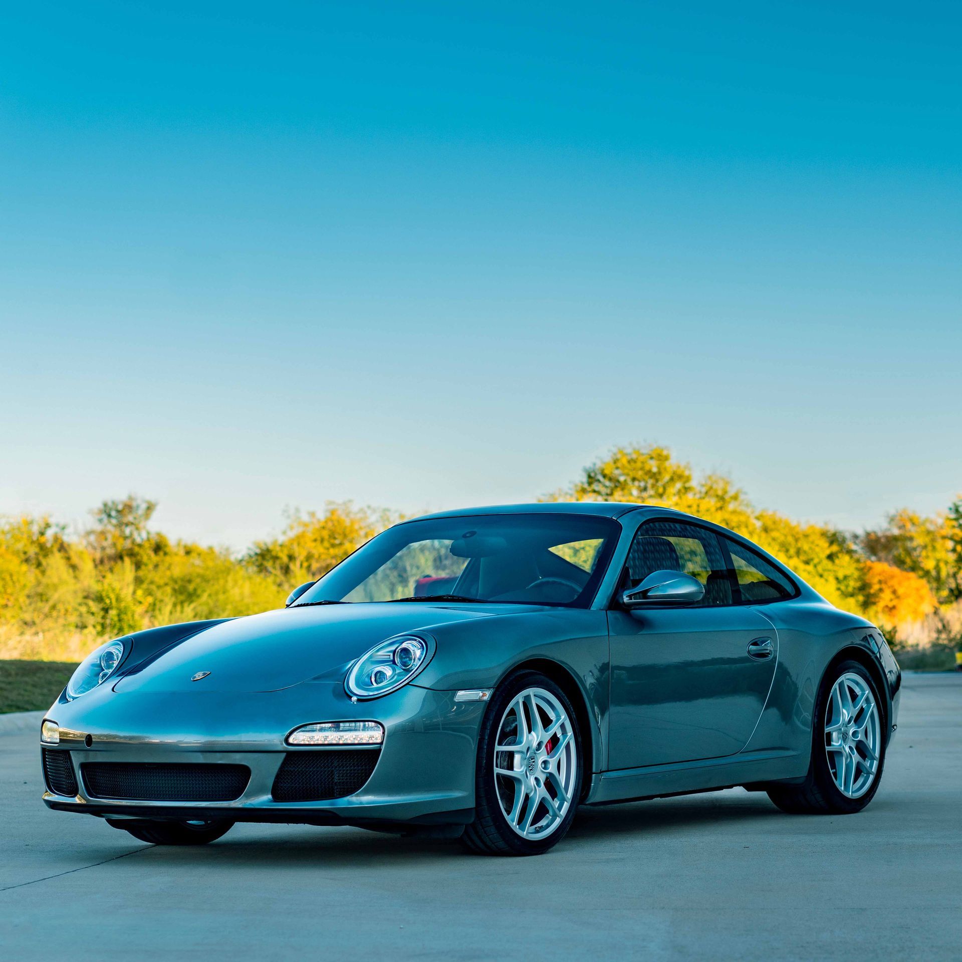 A silver porsche 911 is parked on the side of the road.