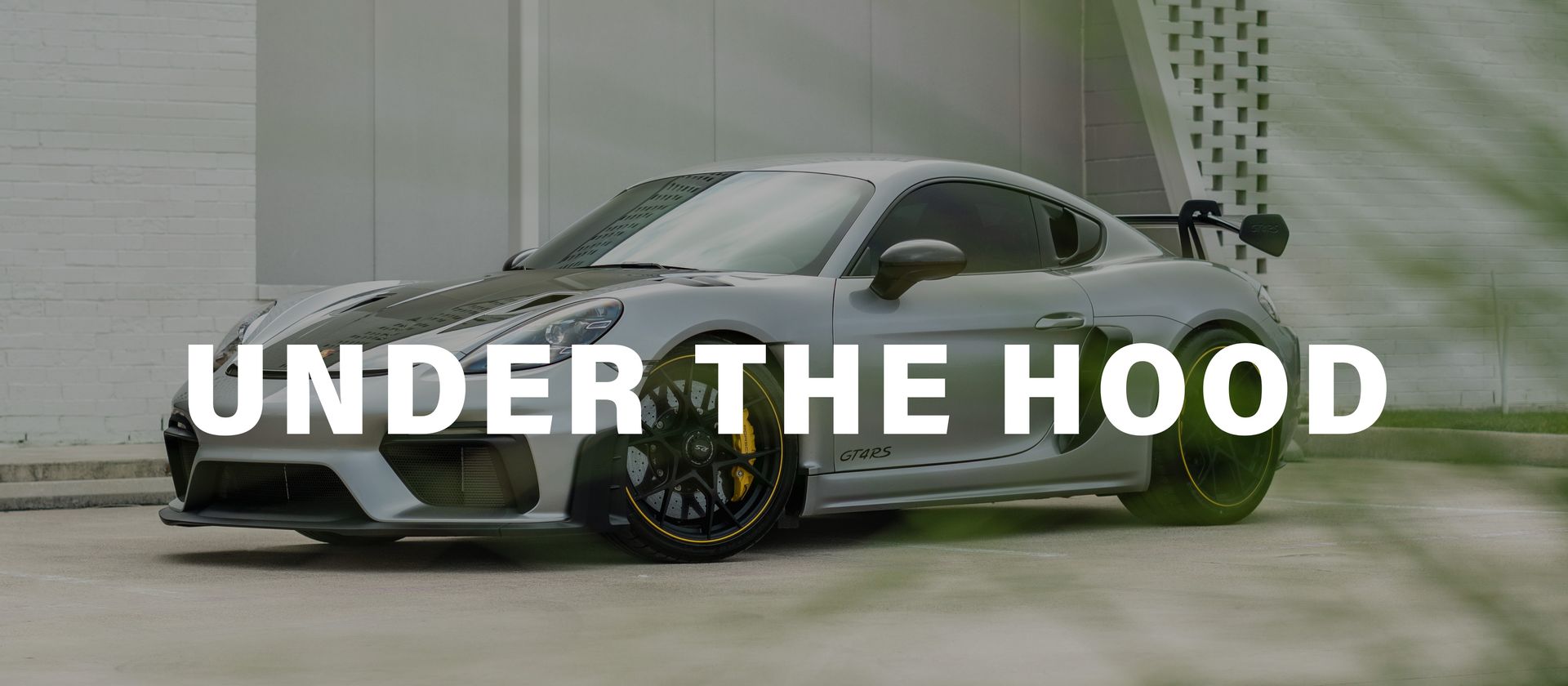 A white sports car is parked in front of a building with the words `` under the hood '' written on it.