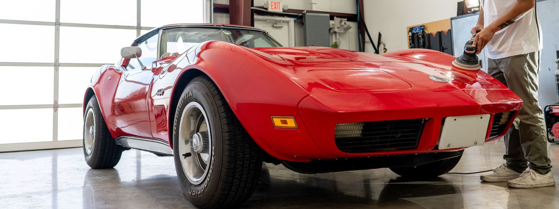 A man is polishing a red corvette in a garage.