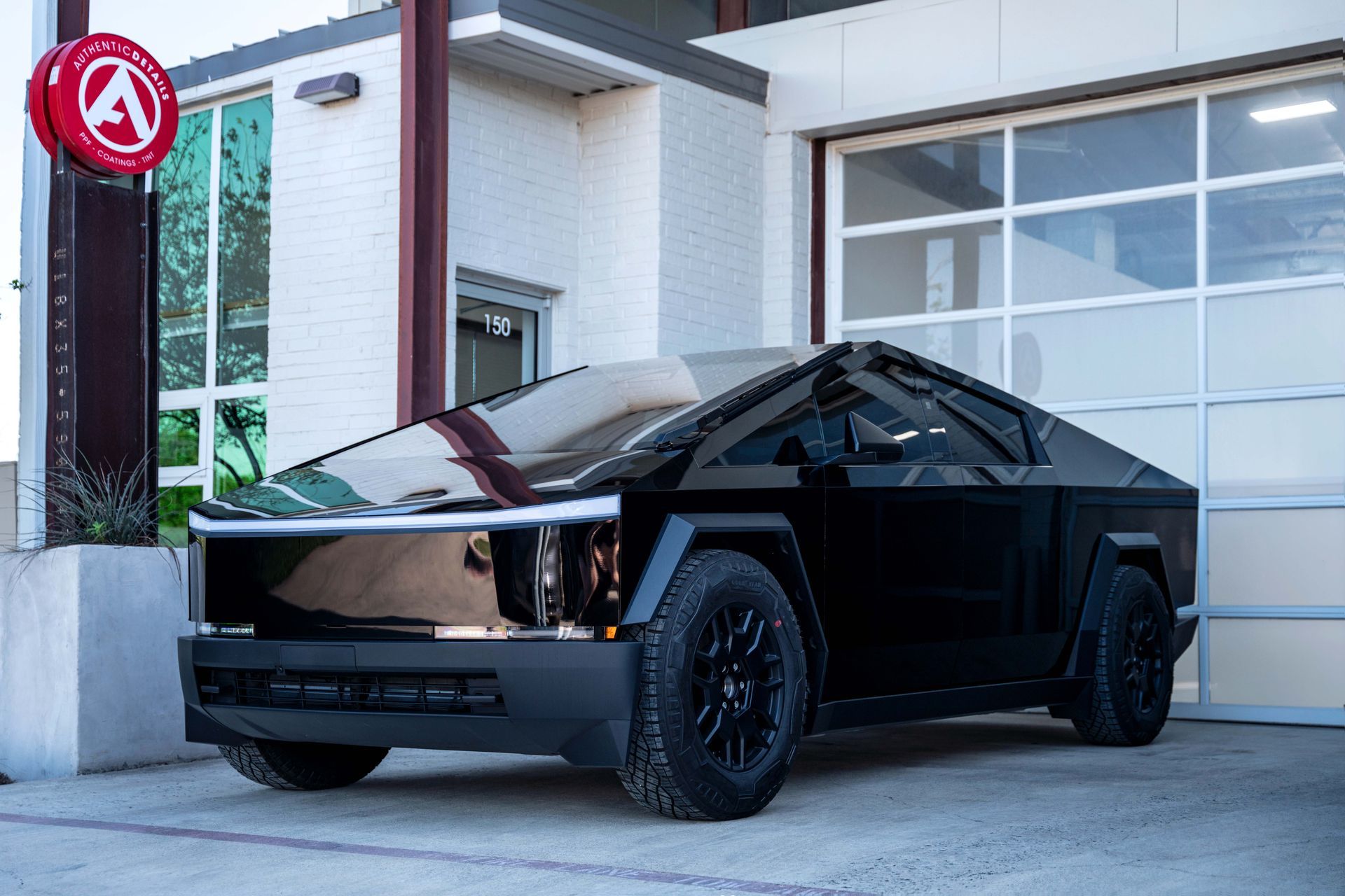 Black Tesla Cybertruck parked in front of a building with a garage door.