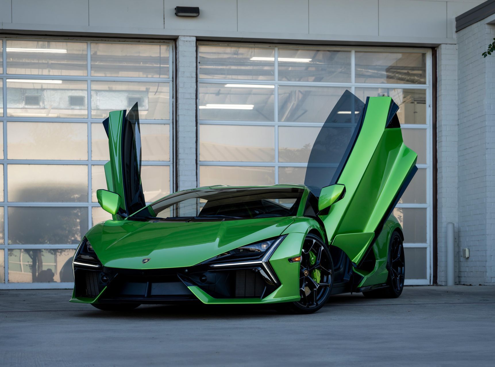 Green sports car with doors open, parked in front of a garage.
