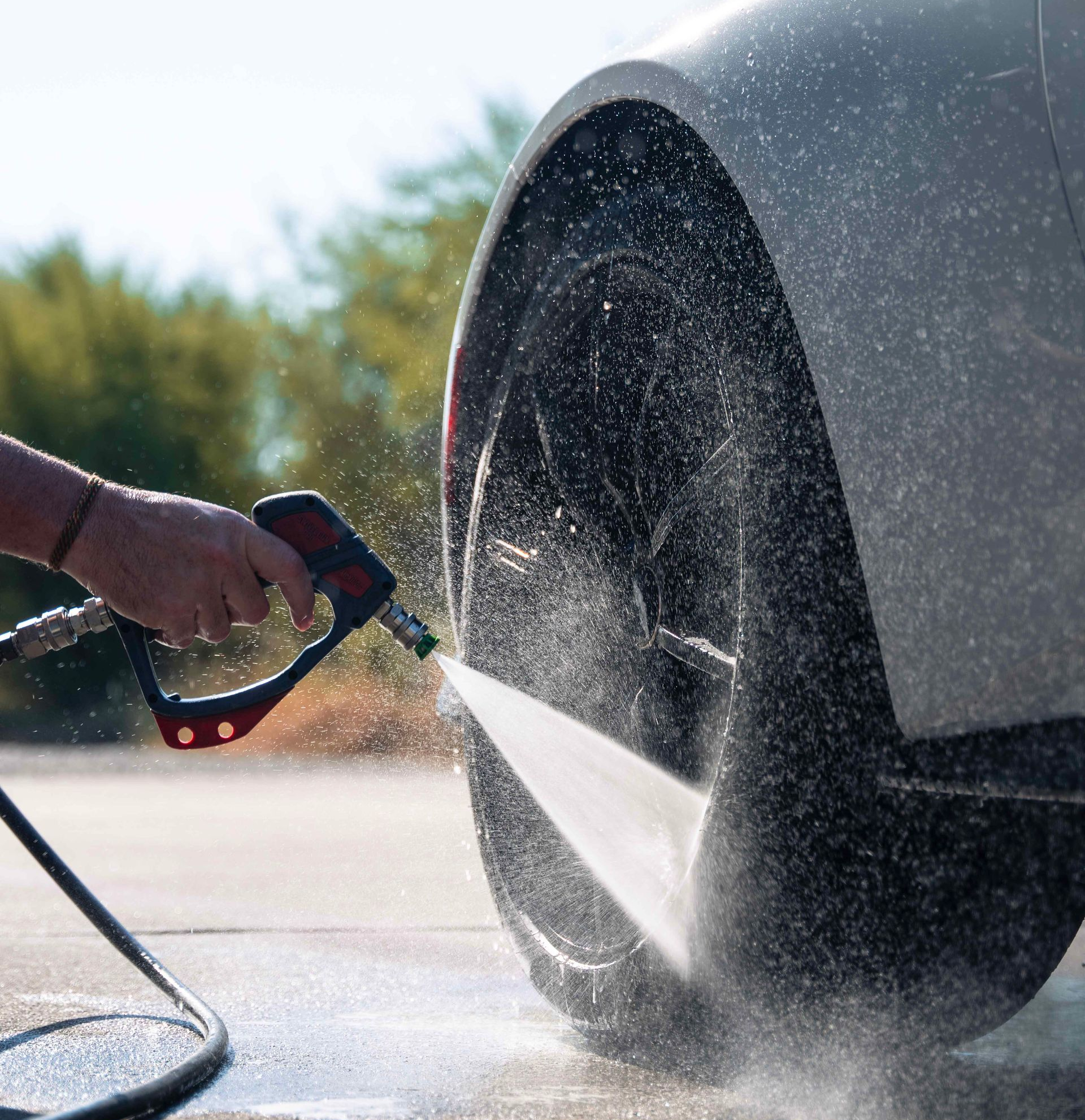 Washing a car tire with a pressure washer; water spray visible.