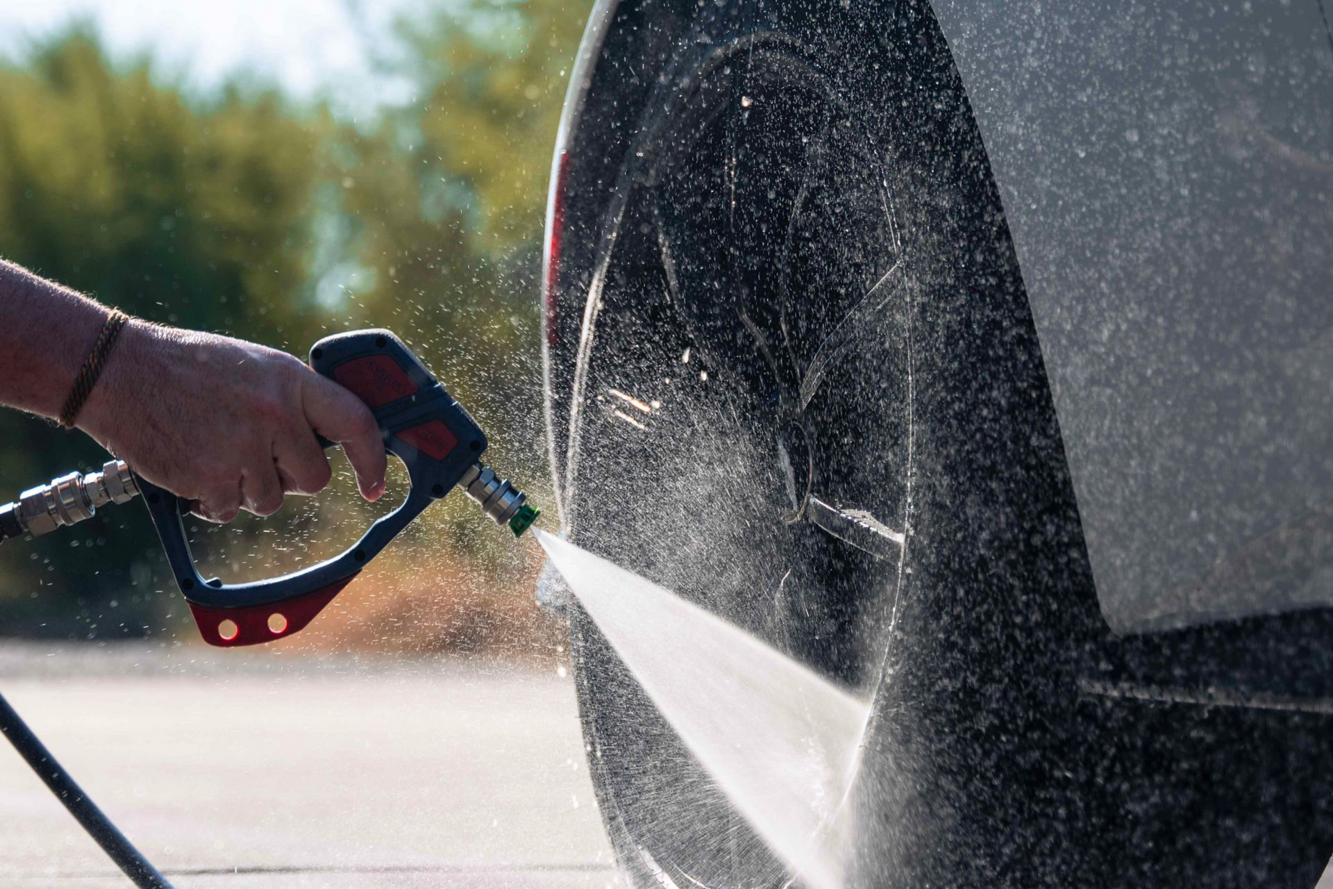 Washing a white car tire with a water hose, water splashing on the pavement.