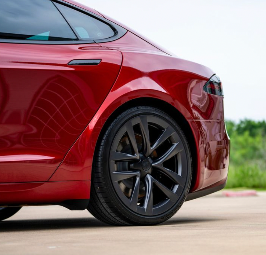 A red car with black wheels is parked on the side of the road