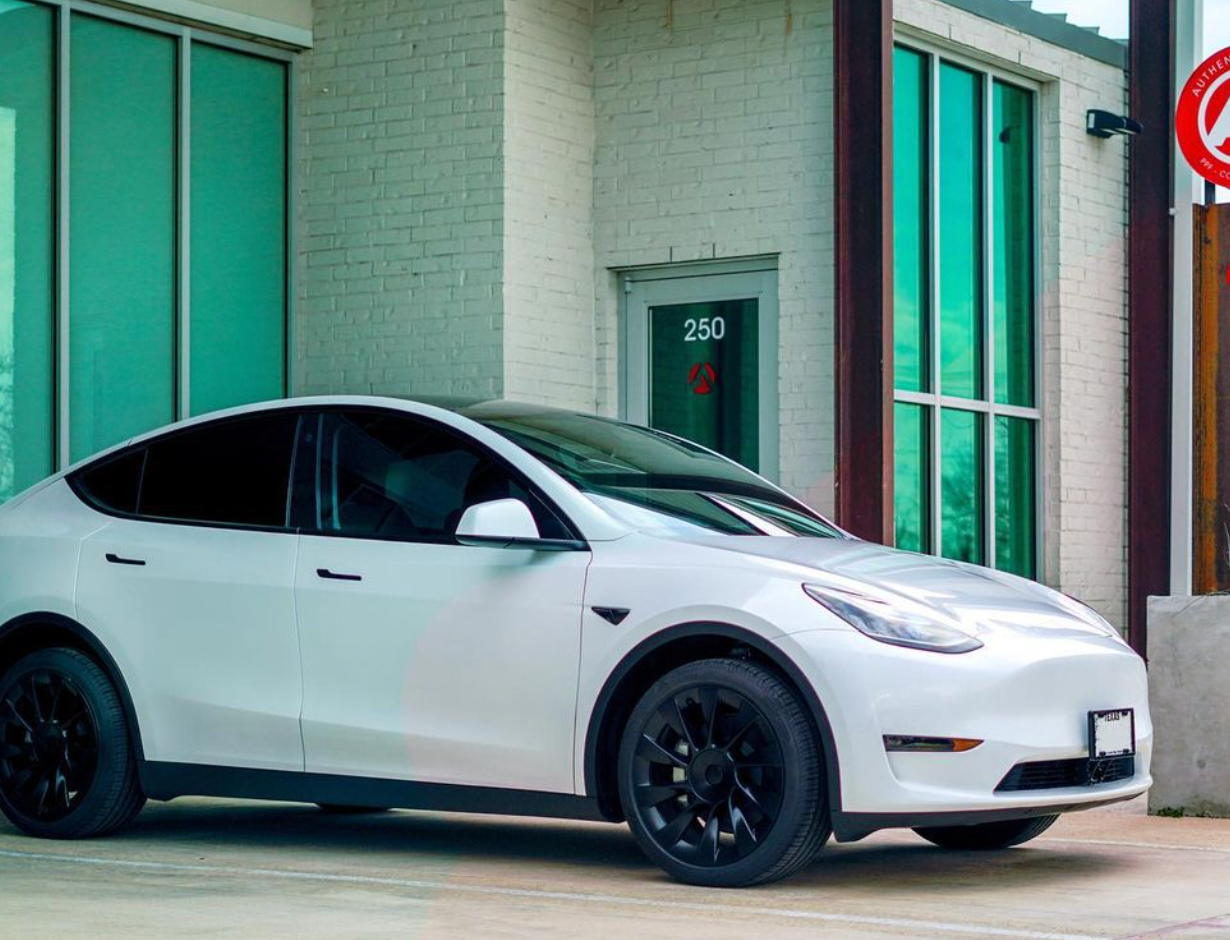 A white tesla model y is parked in front of a building.