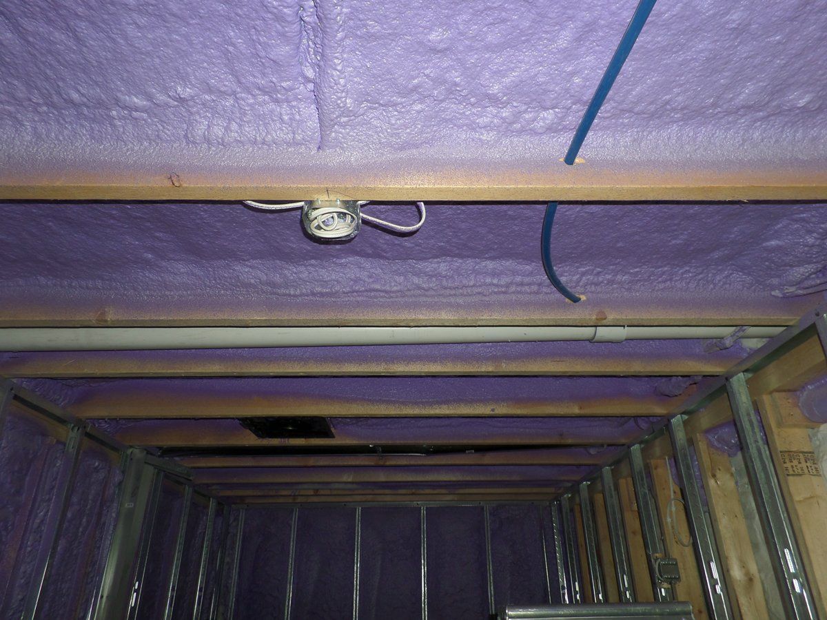 The ceiling of a room with purple insulation and pipes.