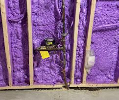 A wall with purple insulation and a pipe in it.