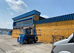 A blue aerial lift is parked in front of a large building.