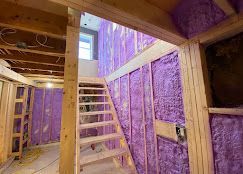 A basement under construction with purple insulation and stairs.