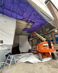 A jlg lift is sitting in front of a building under a blue tarp.