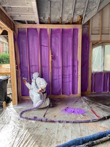 A man is spraying purple insulation on a wall.