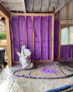 A man is spraying purple insulation on a wall.