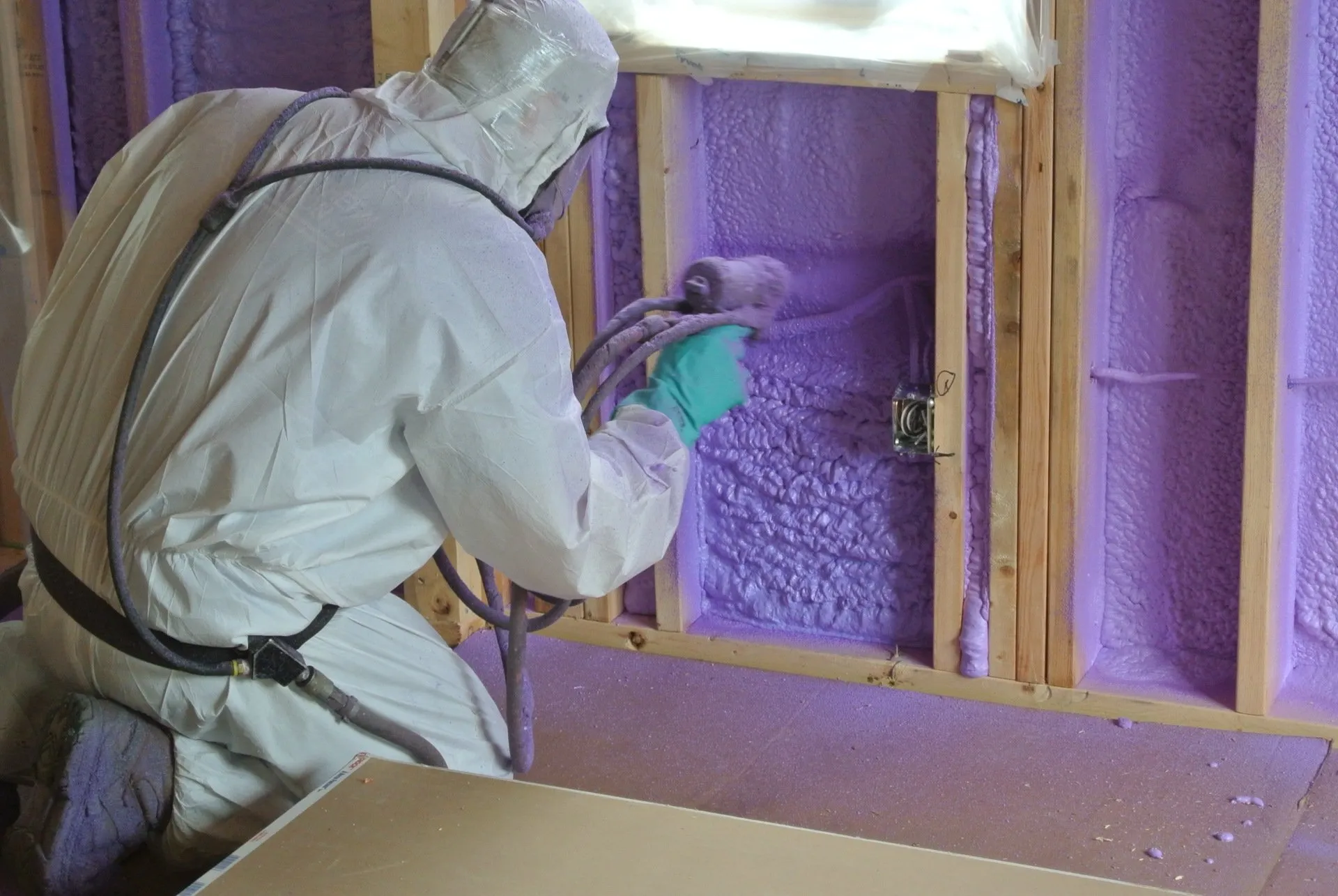 A man in a white suit is spraying purple foam on a wall.