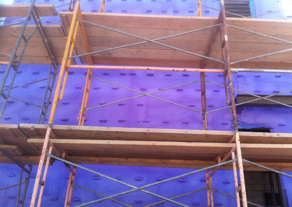 A building under construction with scaffolding and purple insulation