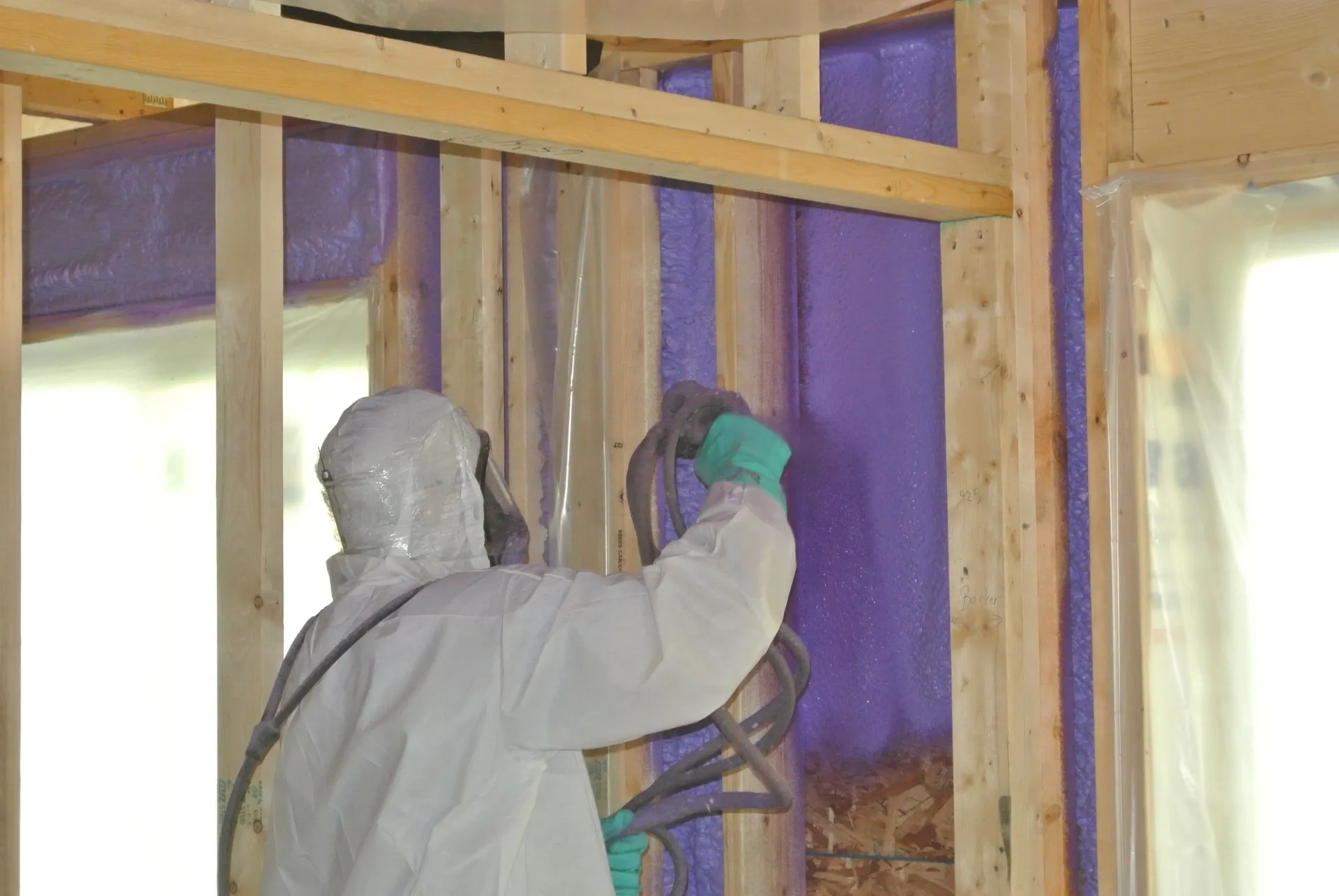 A man in a protective suit is spraying foam on a wall.