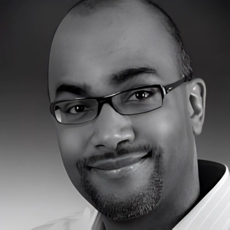 A man with glasses and a beard is smiling in a black and white photo.
