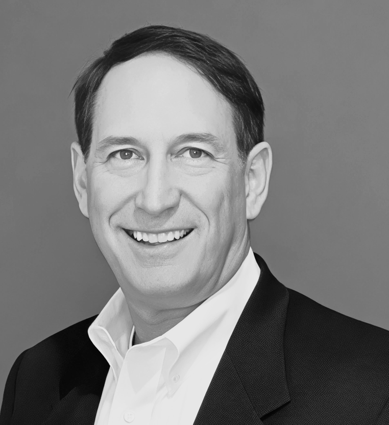 A man in a suit and white shirt is smiling in a black and white photo.