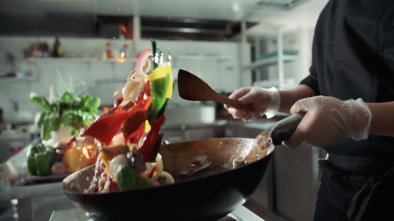 A chef is cooking vegetables in a wok in a kitchen.