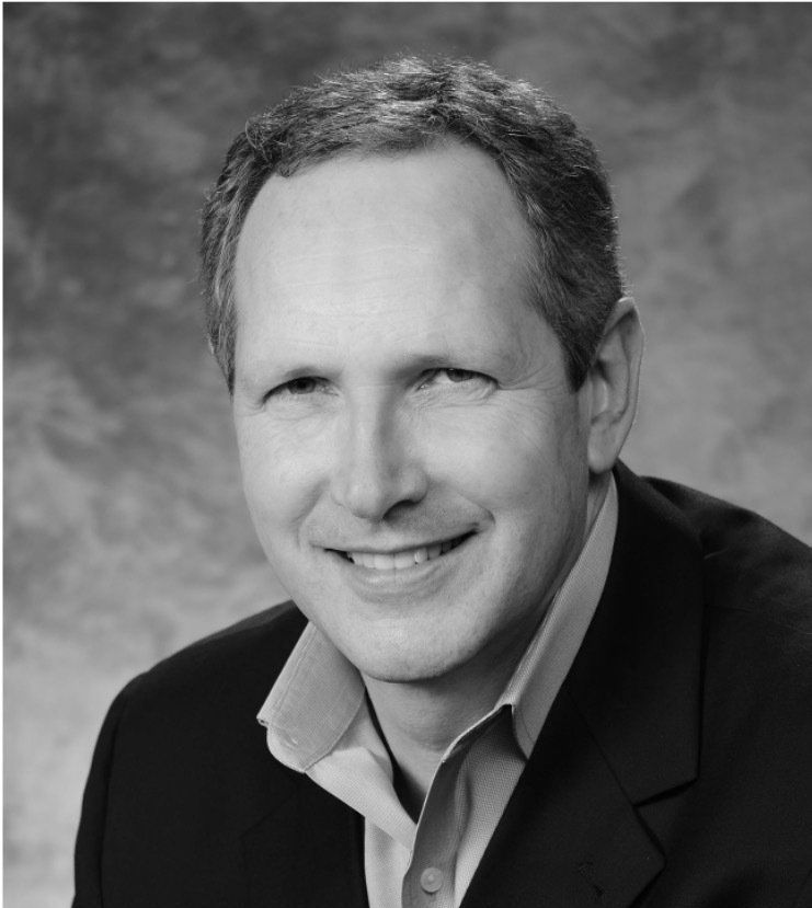 A man in a suit and tie is smiling in a black and white photo