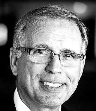 A man wearing glasses and a suit is smiling in a black and white photo.
