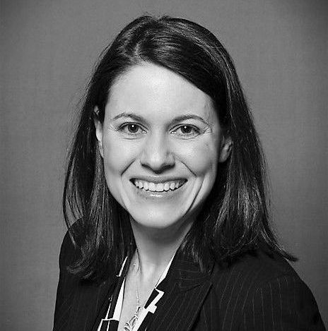 A woman in a suit is smiling in a black and white photo.