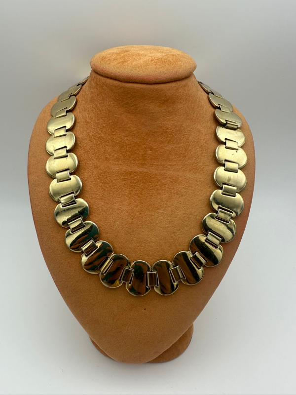 Collana color oro con maglie unite esposta su un busto portagioie color cuoio.