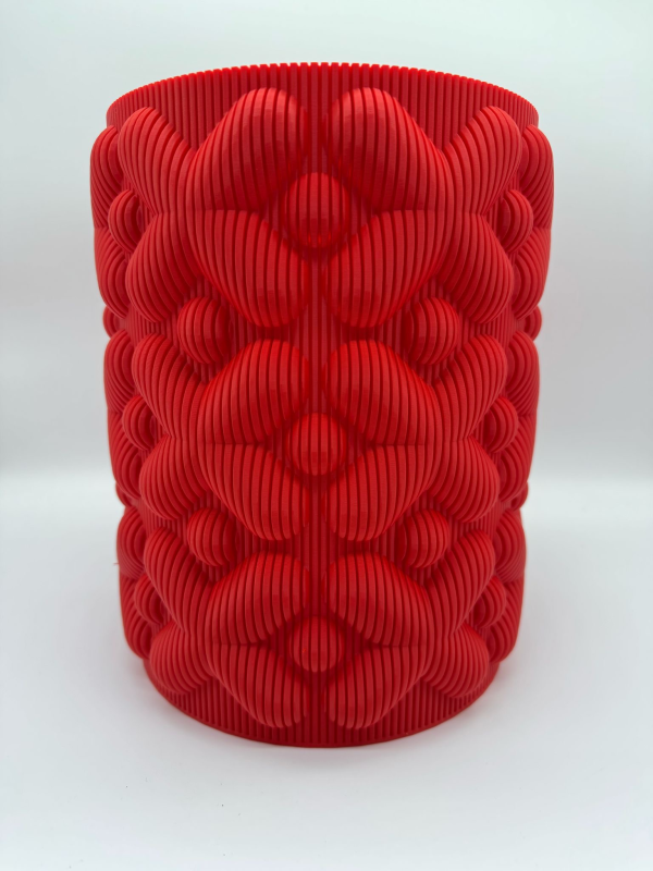 Vaso cilindrico rosso stampato in 3D con motivo floreale strutturato e nervature verticali.