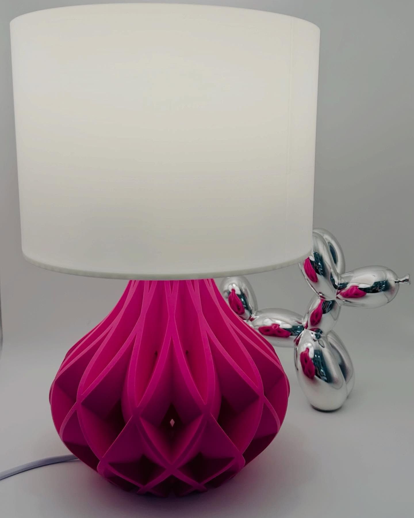 Lampada rosa con paralume bianco, accanto a un cagnolino a forma di palloncino argentato.